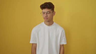 Beyaz tişörtlü, üzerinde ok işareti olan, gülümseyen ve parmakla işaret eden genç İspanyol adam; izole edilmiş sarı arka plan üzerinde dostane ve mükemmel titreşim