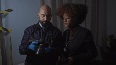 Dedektif gibi davranan bir erkek ve kadın, kapalı alandaki karanlık bir olay yerini araştırıyor, güvenlik kameralarına ve ciddi bir suça işaret ediyor..