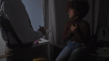 Loş bir odada, bir adam, suç mahalli senaryosu öneren kanıt işaretleri arasında sıkıntılı bir kadını sorgular..