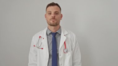 Sakallı, laboratuvar önlüğü, steteskop ve kravatlı kendine güvenen bir erkek doktor beyaz bir duvara dayanıyor..