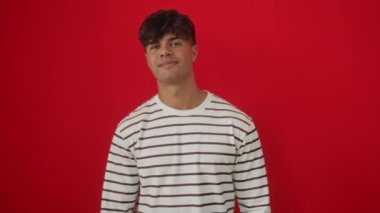 İspanyol asıllı genç adam çizgili tişört giyiyor. Dili dışarıda komik bir ifade sergiliyor. Eğlenceli duygularla dolu izole edilmiş kırmızı arka planda dilini dışarı çıkarıyor.