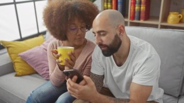 Irklar arası çift evde dinlenir, kadın kahvesini yudumlarken erkek akıllı telefon kullanır.