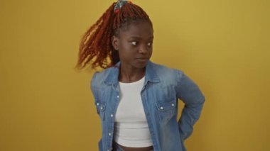 Kot pantolonlu Afrikalı Amerikalı bir kadın, sarı arka planda dikilip fısıldadığı bir sırrı anlatıyor, gizli bir konuşma anı yakalıyor.