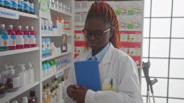 Kendinden emin bir Afrikalı kadın eczacı elinde tabletle dolu bir eczanede duruyor..