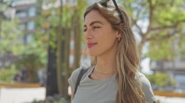Sarışın genç bir kadın yeşil şehir parkında güneşli bir günün tadını çıkarıyor. Rahatlamış ve mutlu bir hava yayıyor..