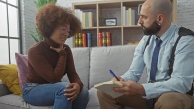 Elinde not defteri olan bir adam, sıkıntılı bir kadını evde bir kanepe ortamında rahatlatır. Destek ve konsültasyon temaları uyandırır..