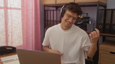 İş yerinde gitar ve davul çalıyormuş gibi yapan, kulaklık takan, beyaz gömlekli, gülümseyen ve müzikten hoşlanan genç bir İspanyol..