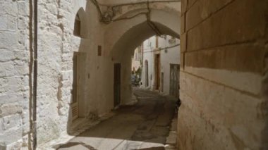 Güneşli bir günde, tarihi Ostuni, Puglia, İtalya 'da taş binalar ve kemerli koridorlarla dolu dar, boş bir sokak..