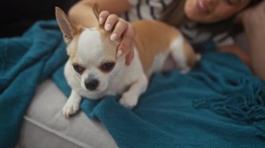 Genç bir kadın, evinde evcil hayvanıyla huzurlu bir anı tasvir etmek için oturma odasında sıcak mavi bir battaniyeye uzanmış, Chihuahua 'sının yanında uzanır..