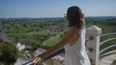 Beyaz elbiseli genç bir İspanyol kadın açık mavi gökyüzü altındaki yeşil kırsal ve tarihi mimariye hayran olan locorotondo, puglia manzaralı bir bakış açısına sahip..