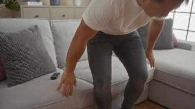 Modern bir oturma odasında evcil köpeğiyle rahat bir kanepede oynayan Asyalı genç bir adam..