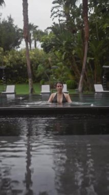 Genç bir kadın, yemyeşil bir yeşillikle çevrili tropikal bir bale otelinde açık havuzda dinleniyor..