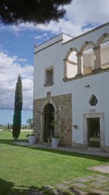 Güneşli bir günde açık havada tarihi italyan villası. Yeşil çimenler, selvi ağaçları ve kemerli taş mimarisi var..