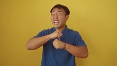 Kızgın genç Çinli adam öfkeli ve kızgın duruyor, hayal kırıklığı içinde bağırıyor ve bağırıyor, izole edilmiş sarı arka plana bakıyor.