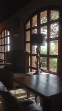 Ahşap bir masa, lamba, deri kanepe, kemerli pencereler ve güneş ışığı içeren zarif bir iç dizayn..