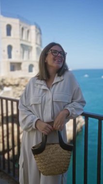 Genç bir İspanyol kadın polignano 'da güzel bir günün tadını çıkarıyor. Bir kısrak, puglia, İtalya, deniz ve tarihi mimari arka planda örülmüş bir el çantası tutuyor..
