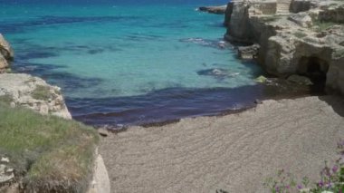 Salento, Puglia, İtalya 'daki şiir mağarası turkuvaz suları, kayalık kayalıklar ve çiçek açan çiçeklerle muhteşem bir plaj sahnesi sergiliyor..