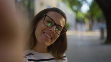 Güneşli bir günde, bulanık bir sokak arkaplanının ortasında gözlük ve çizgili bir gömlek takıp, ders, puglia ve İtalya 'da selfie çekerken gülümseyen genç İspanyol kadın..