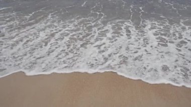 Yumuşak dalgaları ve kumlu sahilde süzülen köpüklü deniz sularıyla sakin bir sahil..