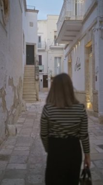 Genç bir İspanyol kadın polignano 'nun pitoresk sokaklarında duruyor. Bir kısrak, puglia, İtalya, gülümsüyor ve büyüleyici beyaz binalarla çevrili dokuma bir çanta tutuyor..