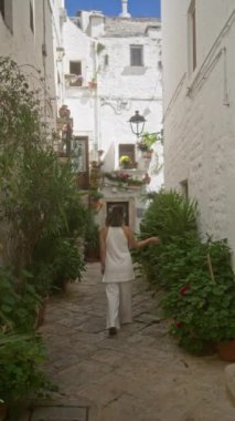 Genç, İspanyol bir kadın locorotondo, puglia, İtalya 'da, güneşli bir günde yemyeşil ve açan çiçeklerle çevrili beyaz yıkanmış yaşlı bir kasabanın büyüleyici sokaklarında geziniyor..