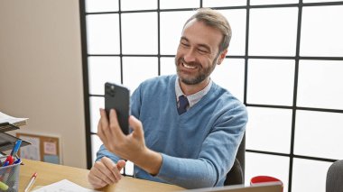 Ofisinde selfie çekerken gülümseyen süveter giyen yakışıklı İspanyol adam..