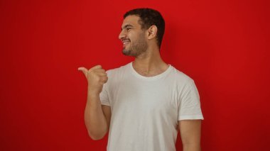 Çekici genç İspanyol adam kırmızı arka planda başparmağıyla işaret ediyor.