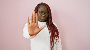 Gözlüklü Afro-Amerikan kadın pembe arka planda poz veriyor, el hareketleriyle duruyor..