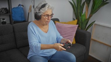 Son sınıf öğrencisi bir kadın, rahat bir oturma odasında kulaklık takıp kumandayla oynamaktan zevk alır..