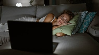Genç bir kadın evdeki kanepede dinleniyor, rahat, loş bir oturma odasında dizüstü bilgisayar izliyor..