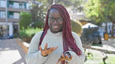 Saçları örgülü gülümseyen Afrikalı kadın şehir parkında gözlük takıyor..