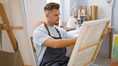 Sanat stüdyosundaki tuvale sakallı, odaklanmış genç bir adam yaratıcılık ve konsantrasyon yayıyor..