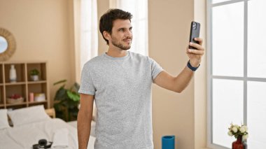 Yakışıklı İspanyol adam rahat bir yatak odasında selfie çekiyor.