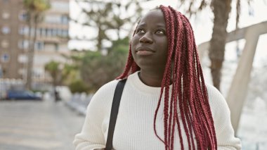 Şehir parkında beyaz kazaklı, dalgın bir Afrikalı kadın..