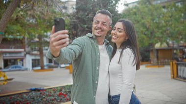 Gülümseyen bir adam ve kadın, şehir sokaklarında birlikte selfie çekiyorlar. Aşkı ve birlikteliği somutlaştırıyorlar..