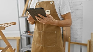 Önlüklü İspanyol adam marangozluk atölyesinde tablet kullanıyor.