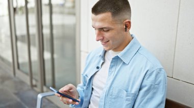 Şehir caddesinde akıllı telefon kullanırken gülümseyen yakışıklı İspanyol bir adam..