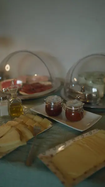 stock image Breakfast buffet featuring various cheeses, jams, meats, olive oil, and condiments displayed under protective covers on a table indoors