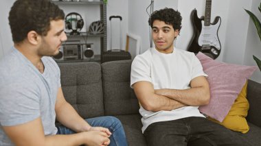 Modern bir salonda arka planda gitarla gelişigüzel sohbet eden iki adam..