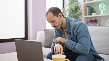 Sakallı İspanyol bir adam oturma odasındaki kanepede oturmuş kol saatini kontrol ediyordu..