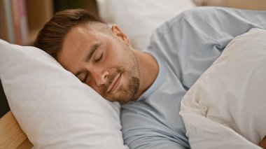 Yakışıklı genç adam, parlak bir yatak odasında, mavi yatak örtüsüyle huzur içinde uyuyor..