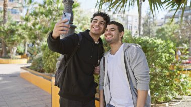 Bereketli bir şehir parkında tropikal yapraklarla selfie çeken iki gülümseyen adam..