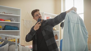 Genç İspanyol bir adam sıradan bir gömlekle bir odada selfie çekiyor, modern bir gardırop sergiliyor..