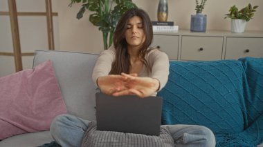Genç bir İspanyol esmer kadın, oturma odasındaki rahat bir koltukta dizüstü bilgisayarıyla otururken esniyor..