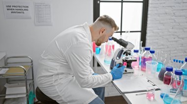 A young caucasian man examines specimens using a microscope in a science laboratory. clipart