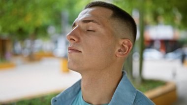 Genç bir İspanyol adam gözleri kapalı rahatlar, nefis yeşil bir park ortamında sükunet yayar, dışarıda huzur taşır..