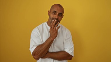 Sarı arka planda poz veren genç Afro-Amerikalı adam düşünceli bir şekilde duygularını dile getiriyor.