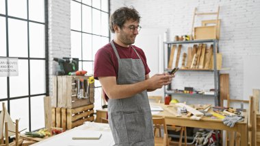 Gözlüklü ve sakallı yakışıklı adam marangozhanedeki telefona bakıyor..
