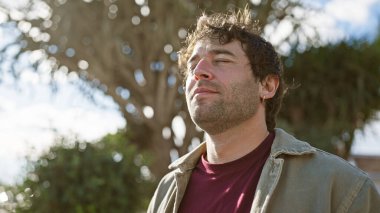 Sakallı dingin bir genç adam açık hava parkında güneşin tadını çıkarıyor..