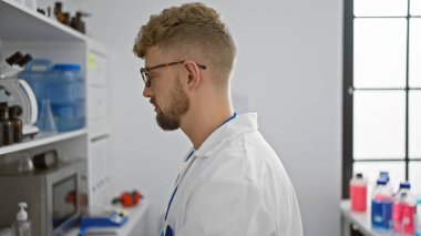 Modern bir laboratuvar ortamında sakallı, gözlüklü ve önlüklü beyaz erkek bilim adamı.